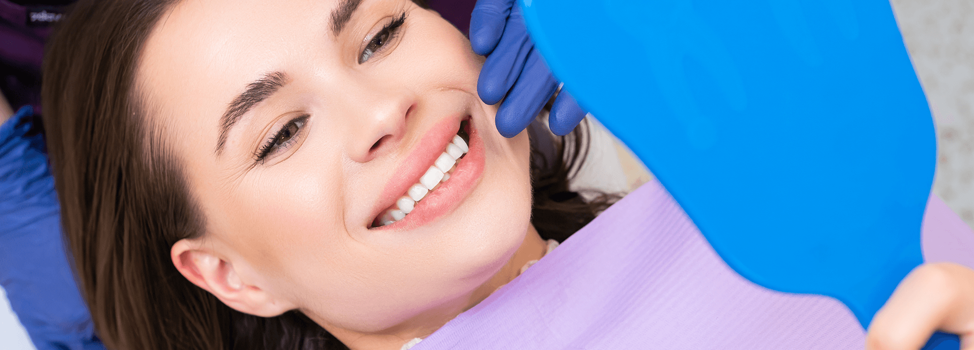 Smiling patient checking her teeth in a hand mirror in the dental chair