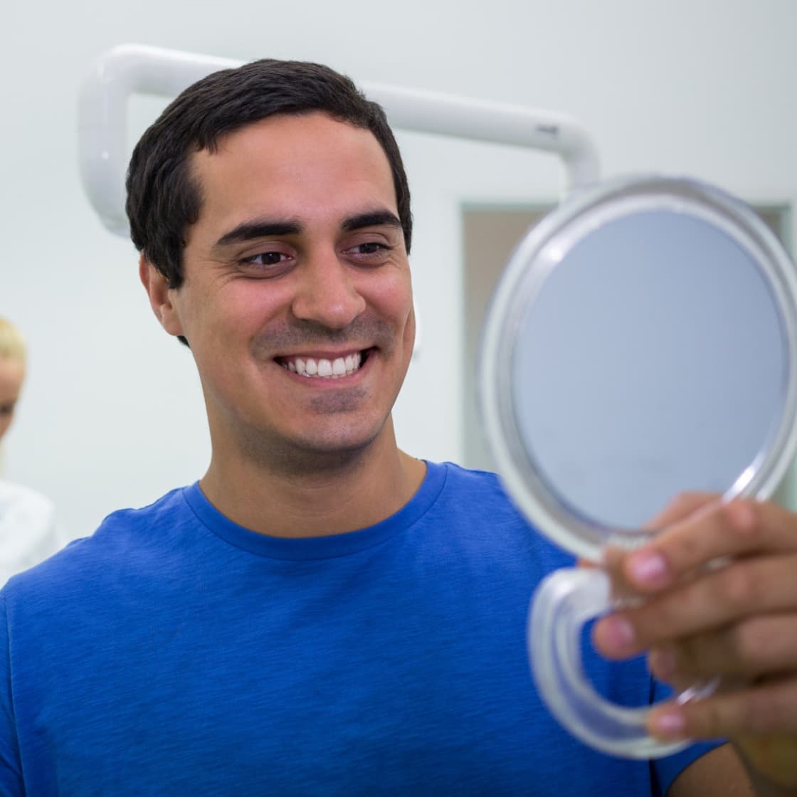 Smiling patient checking his teeth in a hand mirror