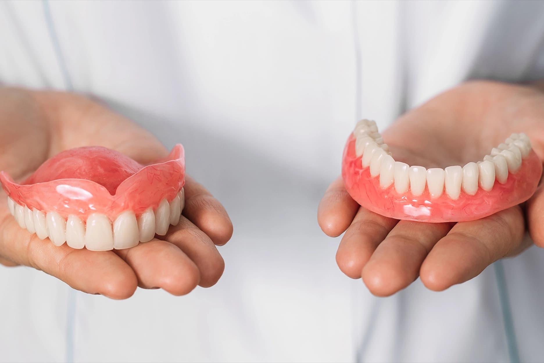 Hands presenting a full set of upper and lower dentures