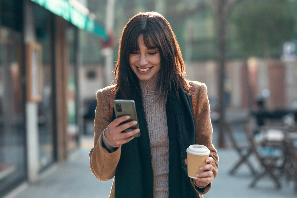 Smiling woman checking her phone while holding a coffee